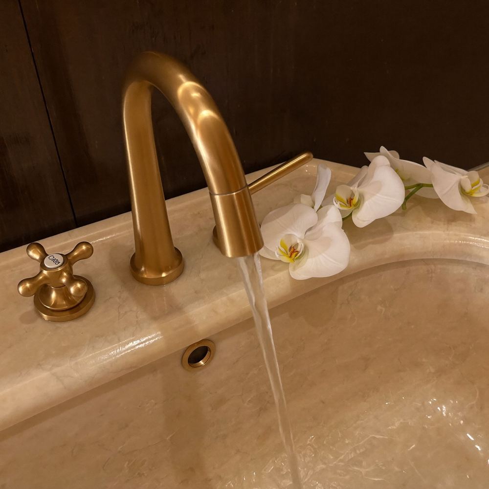 Brushed gold faucet over a marble basin with orchid petals