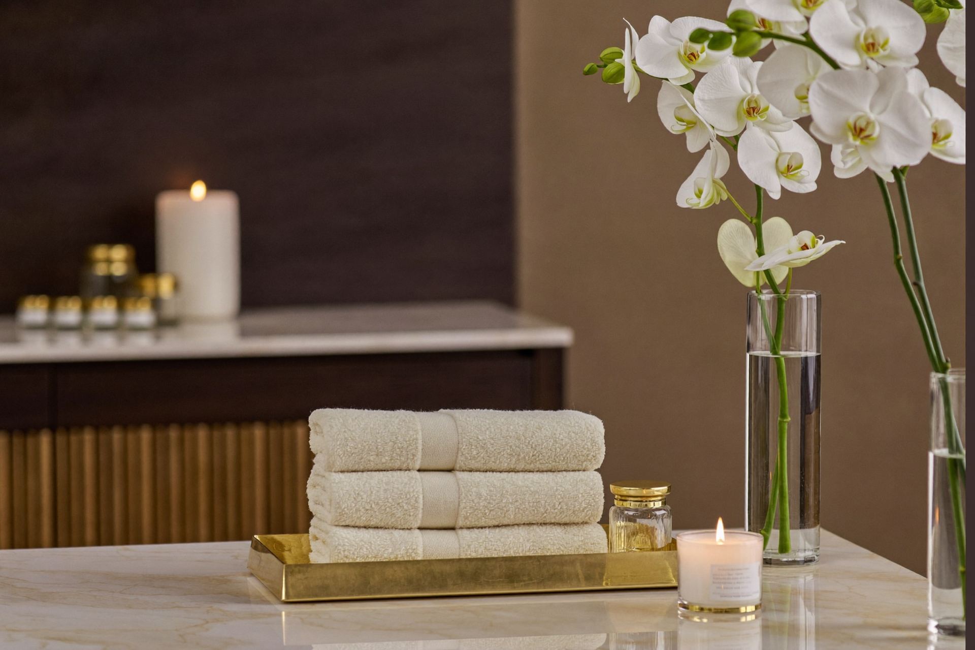 Warm towels on a brass tray beside orchids in Barbara's treatment space